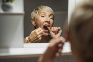 Senior woman flossing her teeth in front of her bathroom mirror