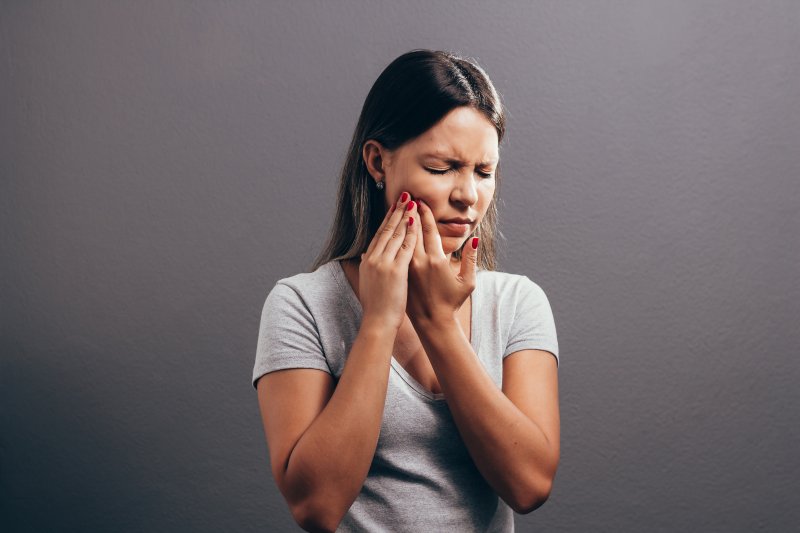 woman experiencing facial pain and holding her cheek 